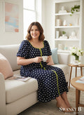 Swanky B Boutique navy blue polka dot midi dress with lime green trim and short puff sleeves, worn by a woman sitting on a couch.